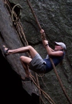 a woman scaling the side of a rock using a vine as a natural rope